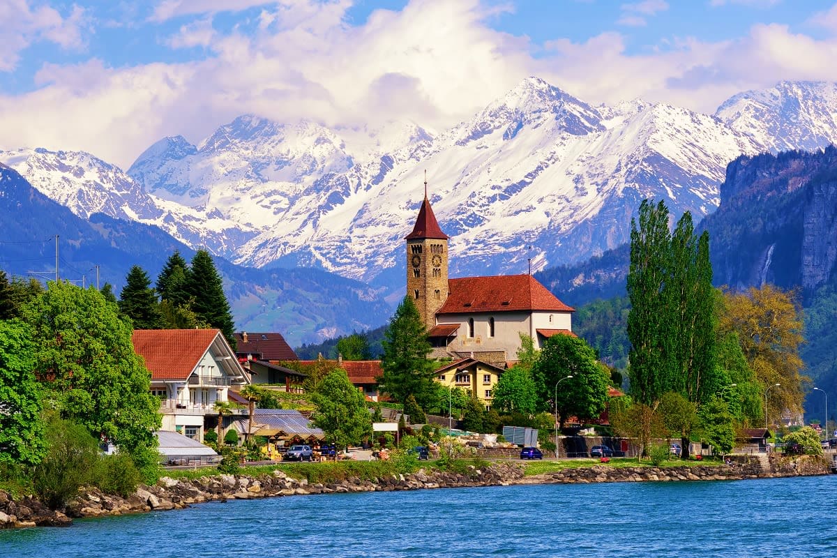 Lakeside Swiss village with church tower overlooking snow-capped Alps and blue water