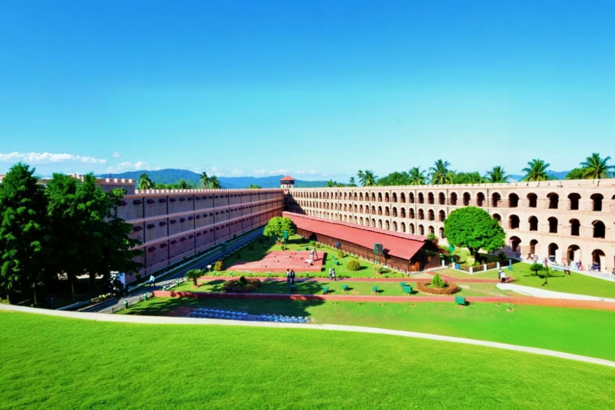 Historic fortress courtyard with manicured grounds, palm trees, and mountain backdrop under clear blue sky