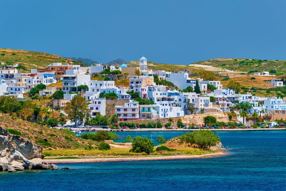 Whitewashed buildings with blue shutters cascading down a hillside to turquoise Aegean waters, typical Greek island architect