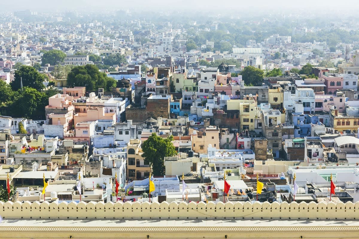 Aerial view of dense Indian cityscape with colorful buildings, temple flags, and hazy skyline stretching to horizon