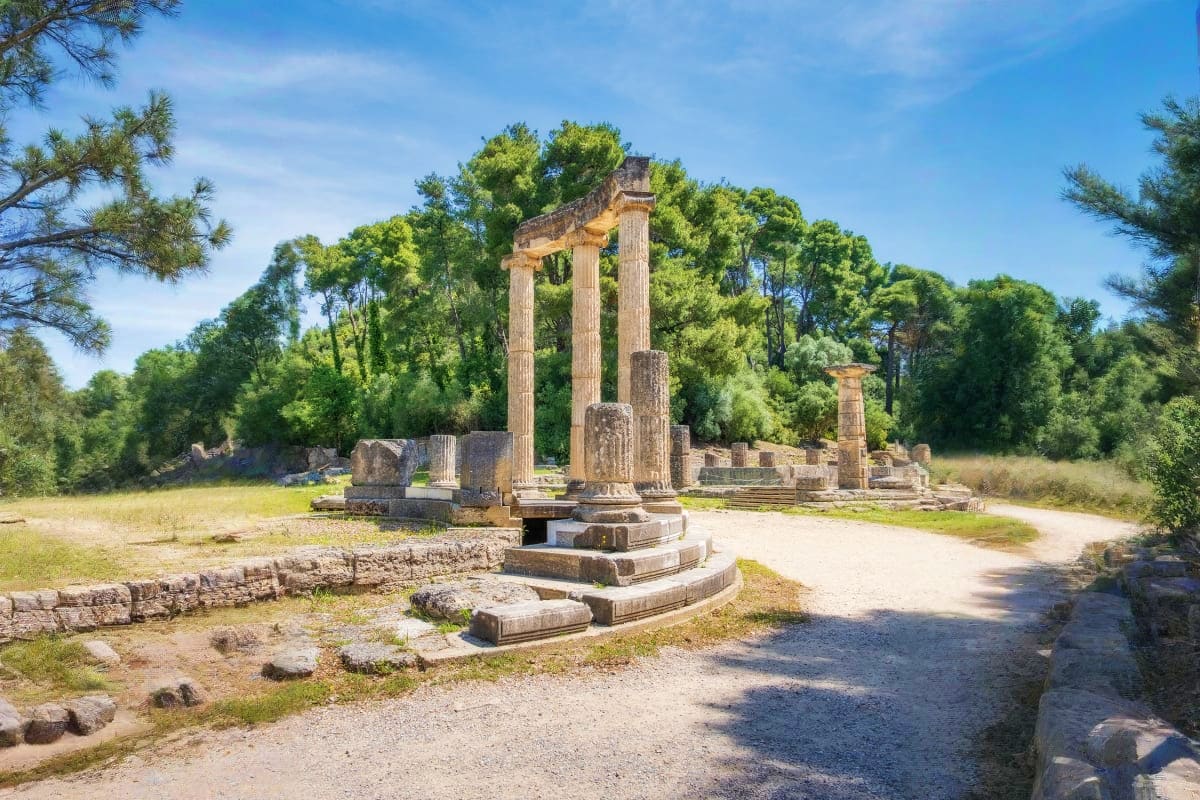 Ancient Greek ruins with three tall Corinthian columns surrounded by pine trees and archaeological remains in Corinth