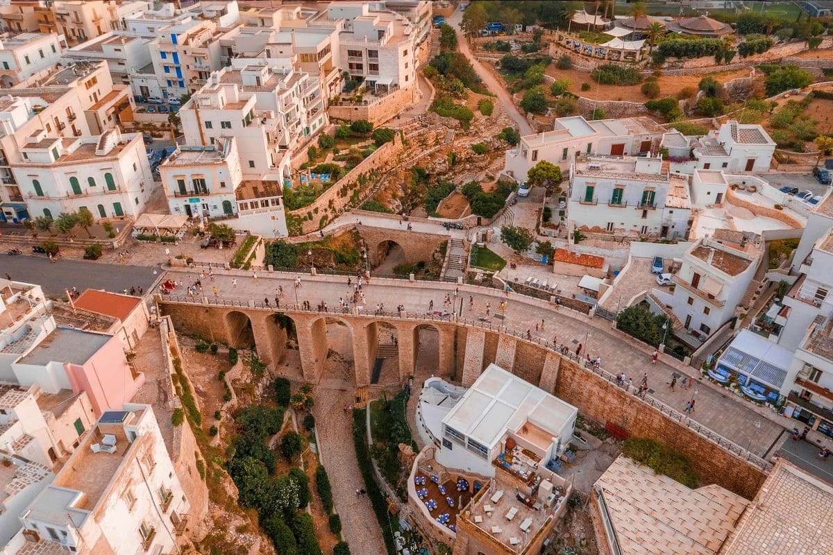 Aerial view of ancient Roman aqueduct with arches spanning valley in Mediterranean hillside town with white buildings and tou
