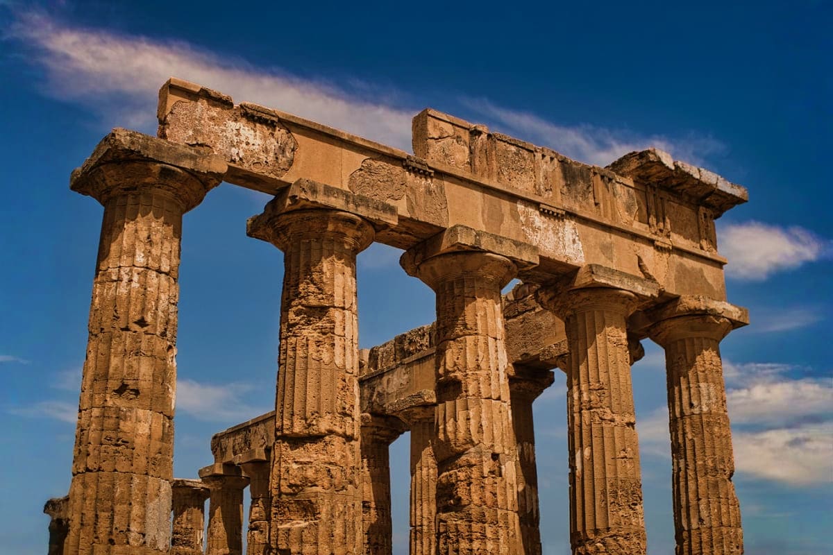 Ancient Greek temple ruins with tall Doric columns and stone architrave against blue sky with clouds