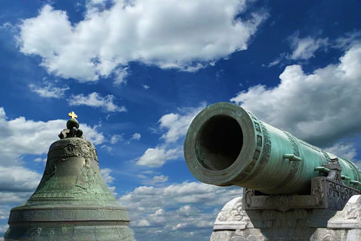 Historic Russian fortress featuring ornate bell tower with golden cross and vintage cannon against blue sky with white clouds