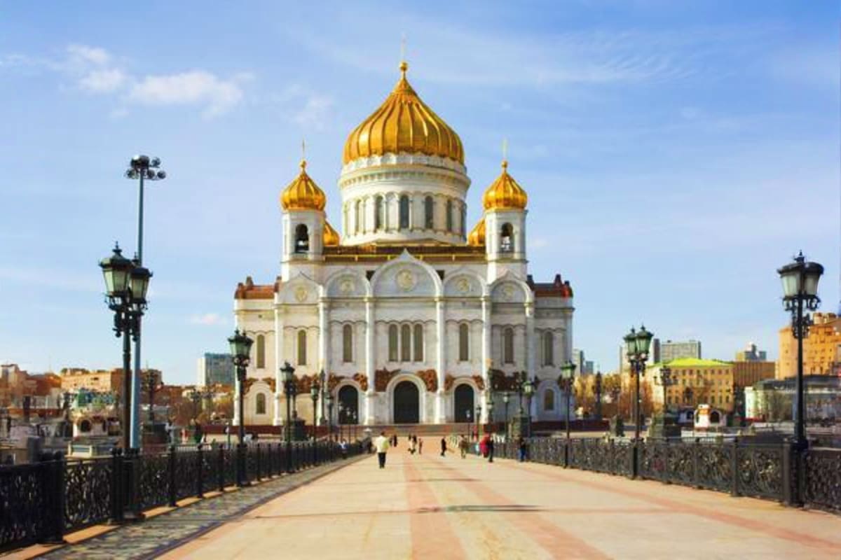 Cathedral of Christ the Savior in Moscow with golden domes, white stone exterior, and pedestrians on bridge approach