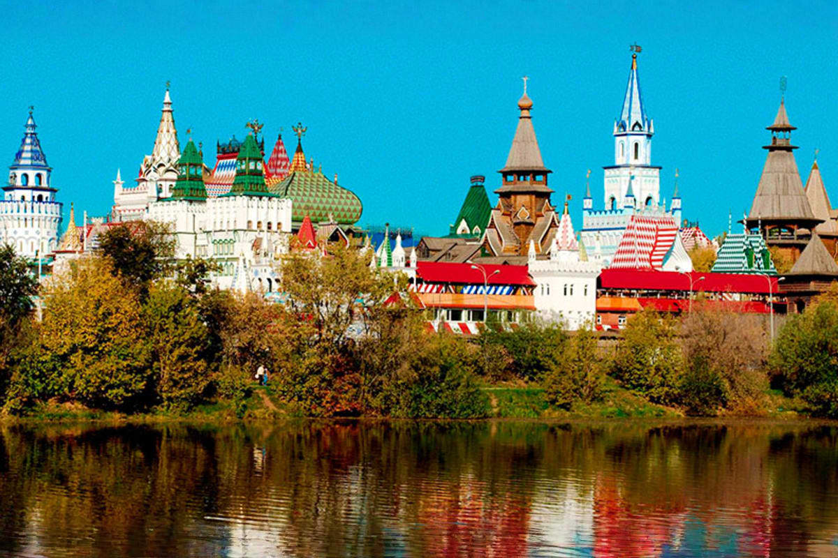 Russian Orthodox churches and colorful traditional architecture reflected in river under blue sky with autumn trees