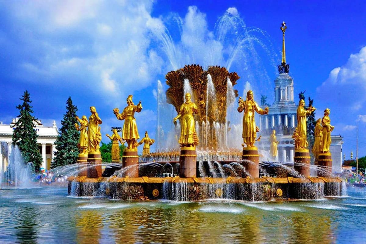 Golden statues of women surrounding ornate fountain with water jets at VDNKh exhibition center in Moscow, Russia, with white 