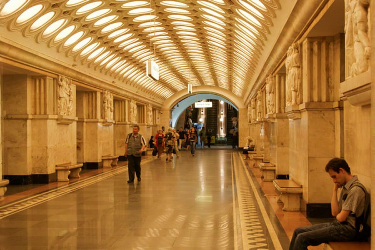 Ornate subway station with cream-colored arched ceiling, decorative columns, and skylights with passengers walking through th