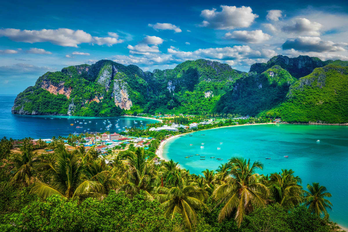 Aerial view of Phi Phi Island Thailand with turquoise waters, limestone cliffs, white sand beach, palm trees and moored boats