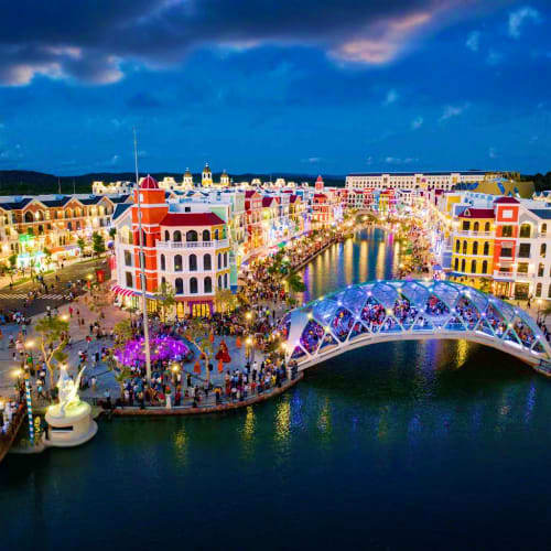 Colorful waterfront buildings and illuminated bridge over canal at dusk in Vietnamese resort town