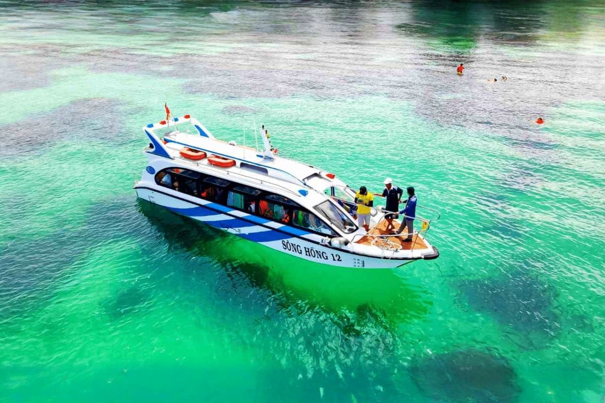 White and blue speedboat named Song Hong 12 anchored in turquoise waters with passengers boarding, tropical island scene with