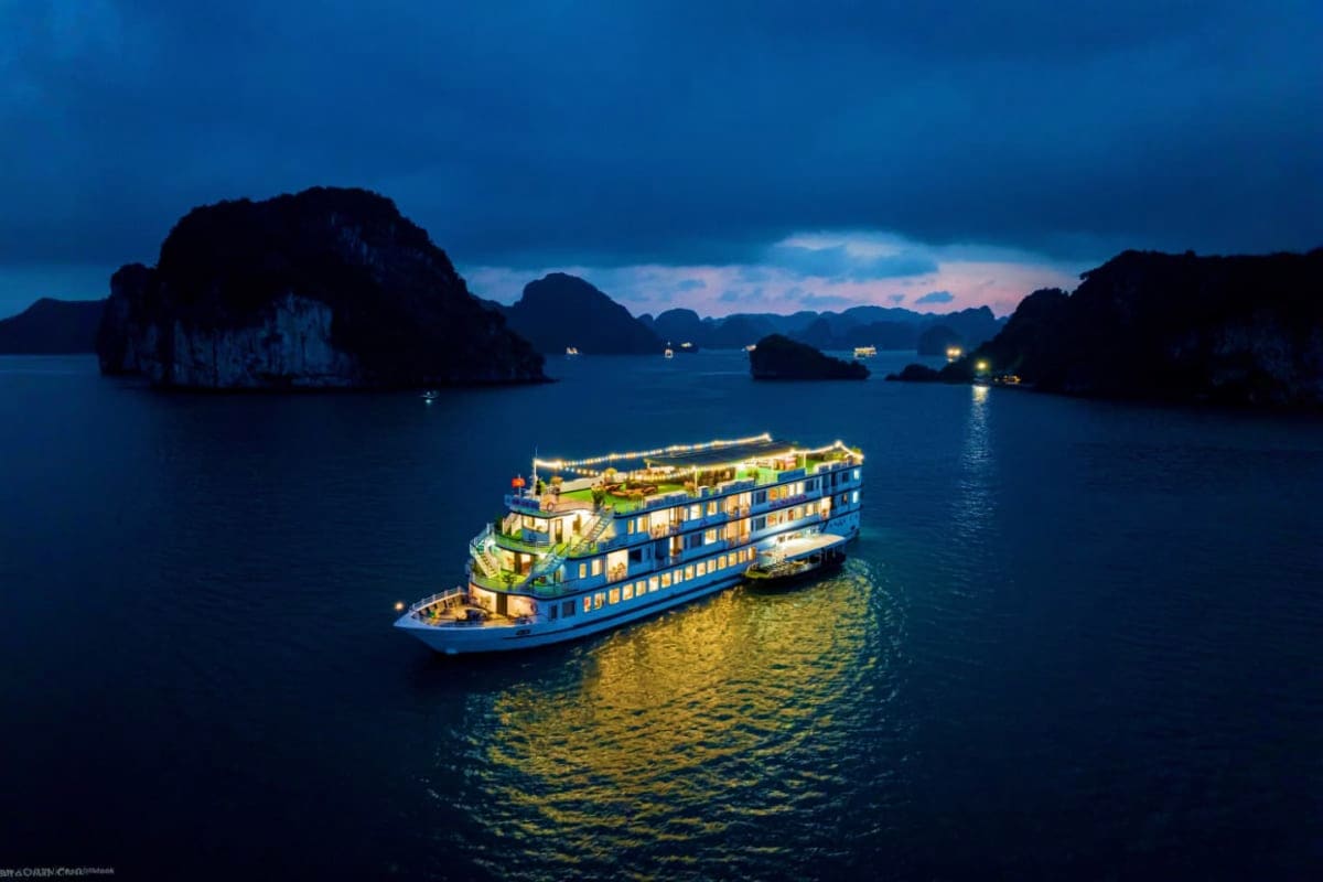 Luxury cruise ship illuminated at dusk in Halong Bay with limestone karst islands silhouetted against twilight sky