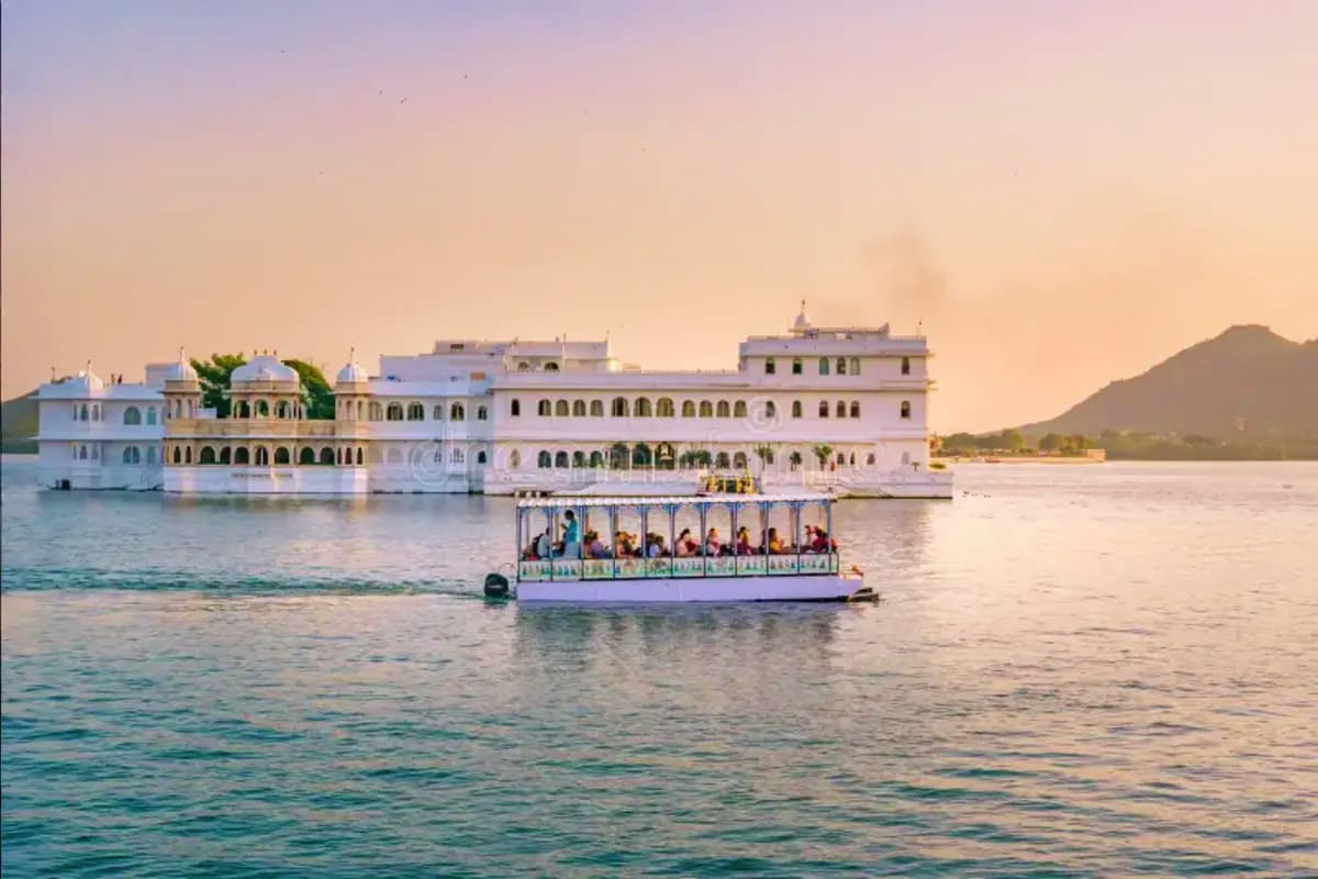 Tourist boat with passengers on Lake Pichola in front of the white marble Lake Palace hotel in Udaipur, Rajasthan at sunset
