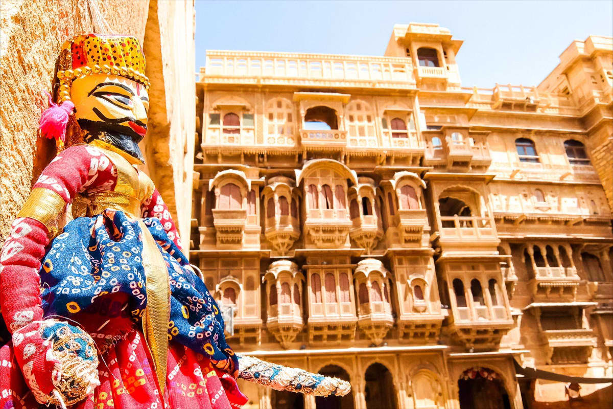 Colorful Indian puppet doll in traditional dress displayed against ornate golden sandstone palace architecture in Jaisalmer, 