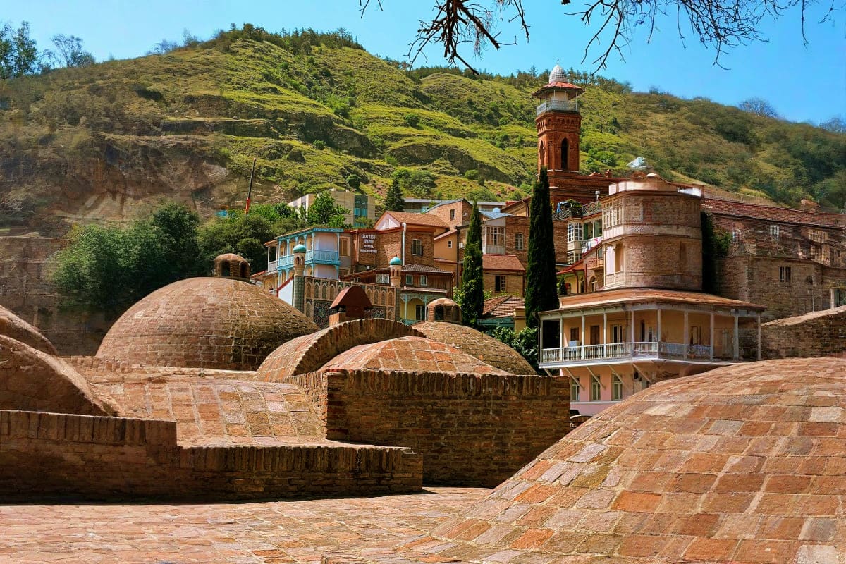 Historic sulfur baths with traditional domed structures and minaret tower nestled against green hillside in Tbilisi, Georgia
