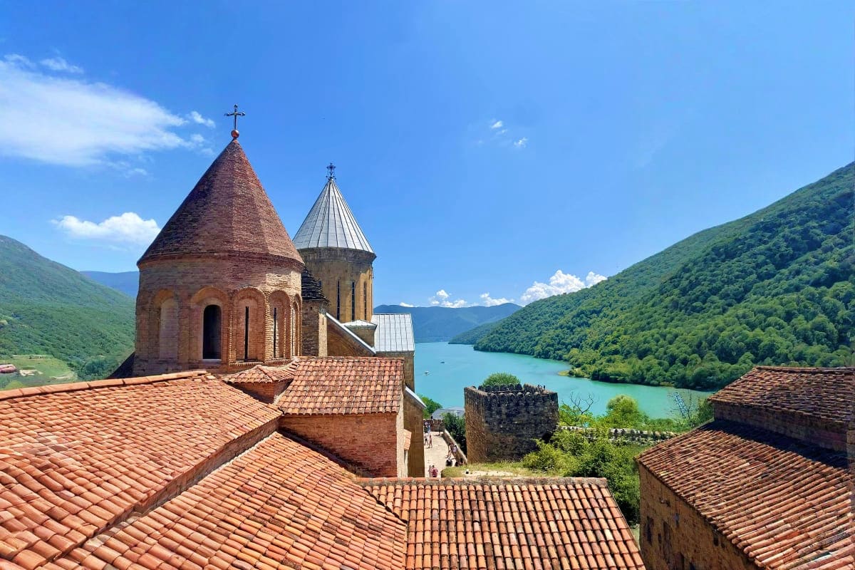 Ancient Armenian monastery with stone domes and red tile roofs overlooking turquoise lake and green mountains in Georgia
