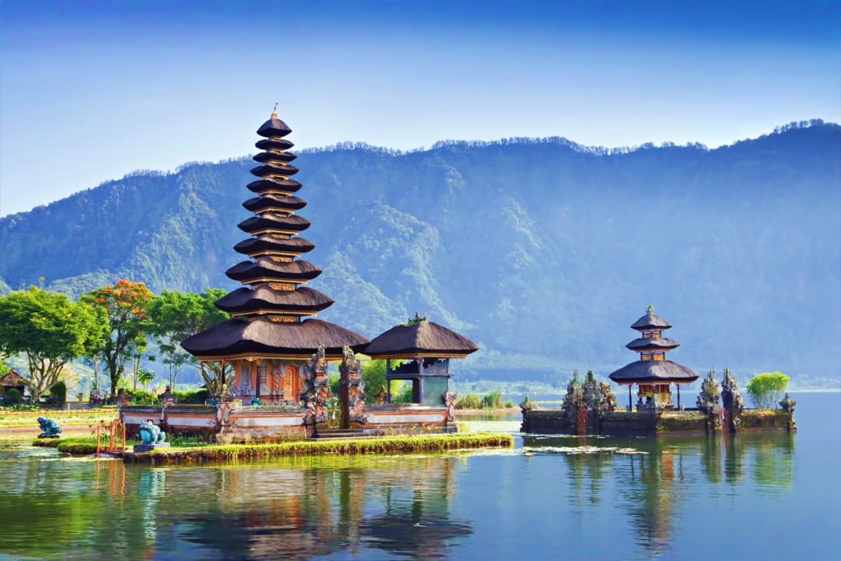 Pura Ulun Danu Bratan temple with tiered roofs reflected in lake water, forested mountains in background, Bali Indonesia