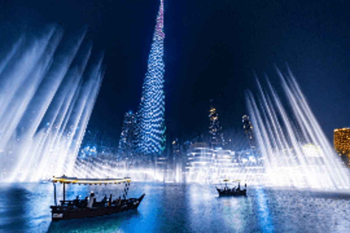 Dubai Fountain illuminated at night with traditional abra boats on the water and illuminated skyscrapers in the background