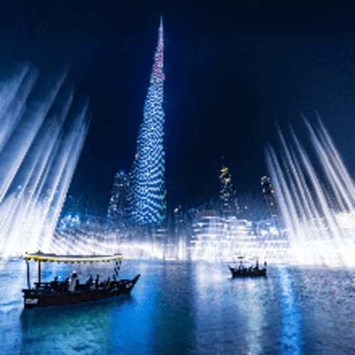Burj Khalifa illuminated at night with fountain show and traditional abra boats on Dubai water