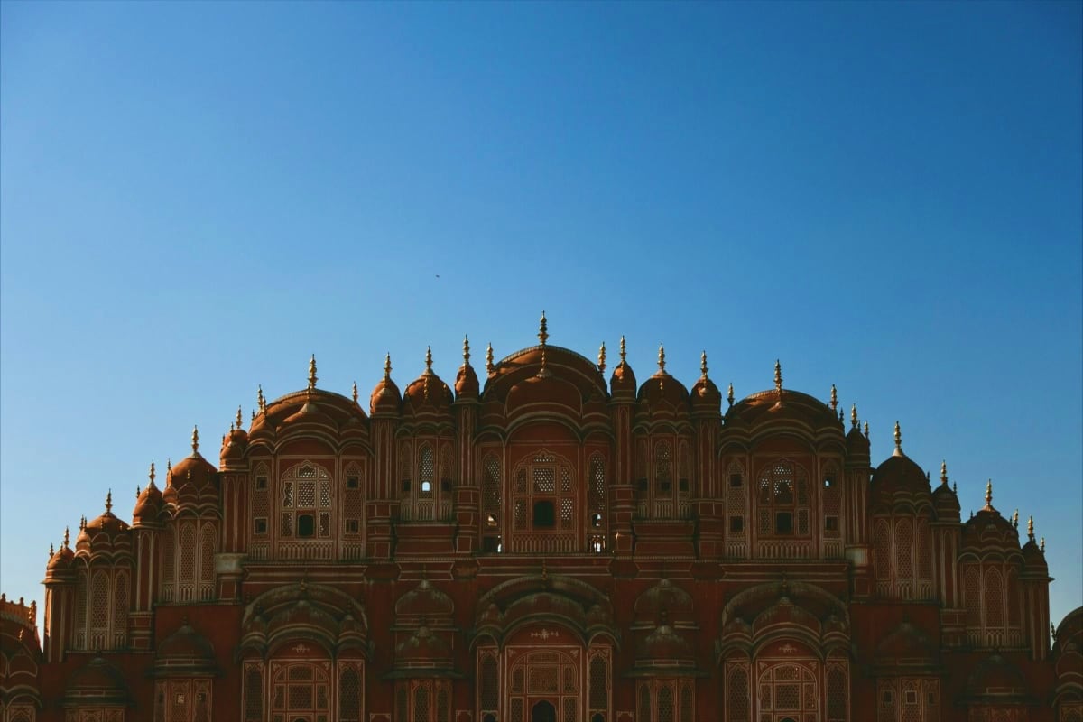 Historic ornate red sandstone palace with golden domed towers and intricate architectural details against clear blue sky