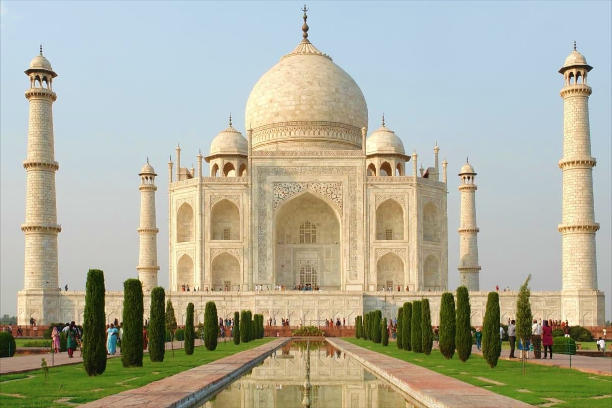 Taj Mahal with reflecting pool, minarets, cypress trees, and visitors in Agra, India