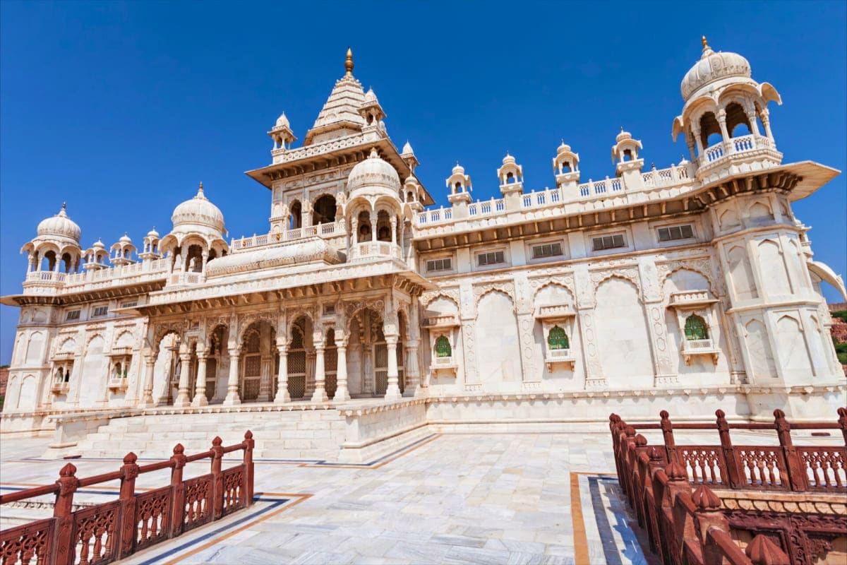 White marble Sikh temple with multiple domes and ornate architecture under blue sky, featuring carved railings in foreground