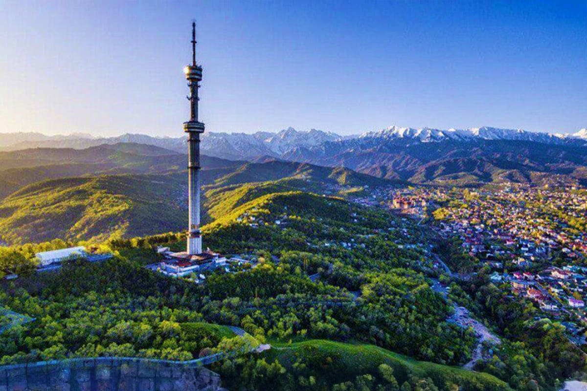 Chimbulak Tower rising above forested mountains and valley with snow-capped peaks in the distance, Almaty Kazakhstan