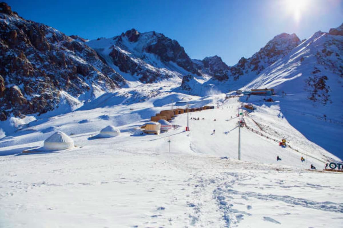 Snow-covered ski resort nestled in mountain valley with ski lifts, lodges, and snow-capped peaks under clear blue sky