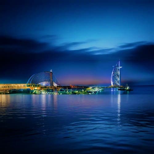 Dubai waterfront at dusk showing illuminated Burj Al Arab and Jumeirah Beach Hotel reflected in calm Arabian Gulf waters