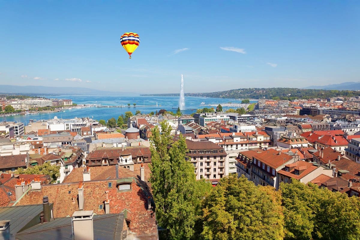 Hot air balloon flying over Lausanne cityscape with Lake Geneva and Jet d'Eau fountain visible in background