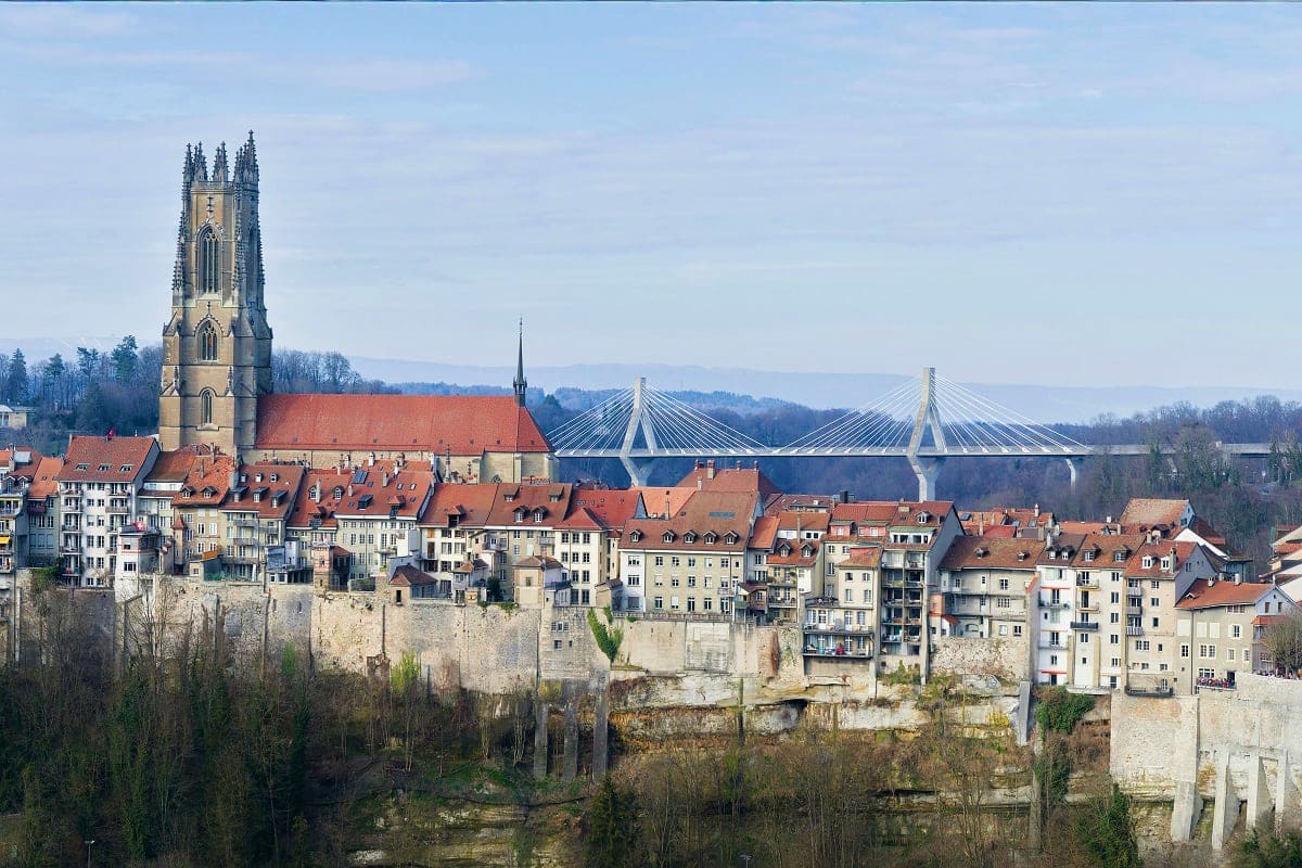 Medieval city of Bern with Gothic cathedral tower, red-roofed buildings, stone fortifications, and modern cable-stayed bridge