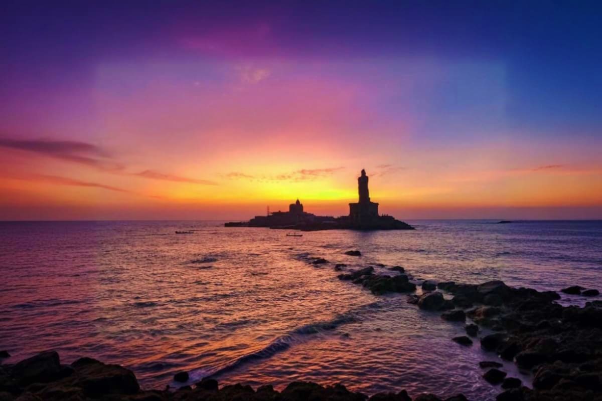 Lighthouse silhouetted against golden sunset over rocky coastline and ocean waters at dusk