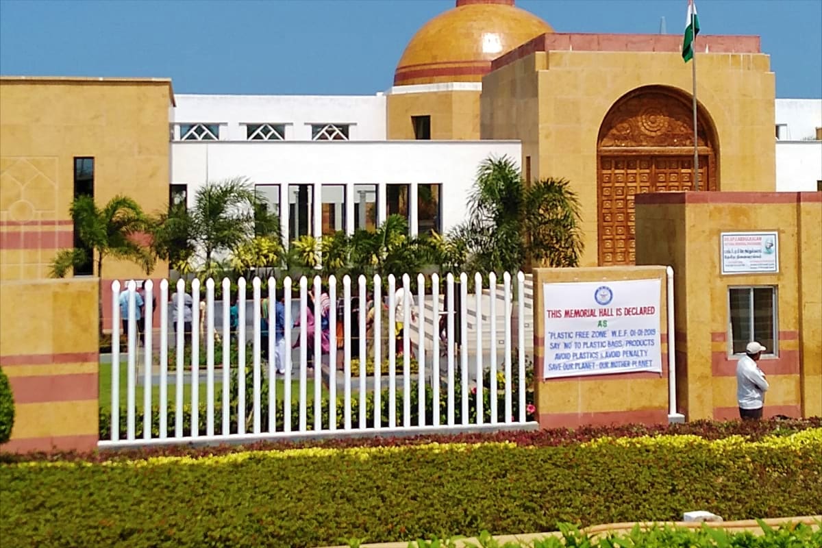 Indian memorial building with golden dome, white gate, and palm trees under clear blue sky