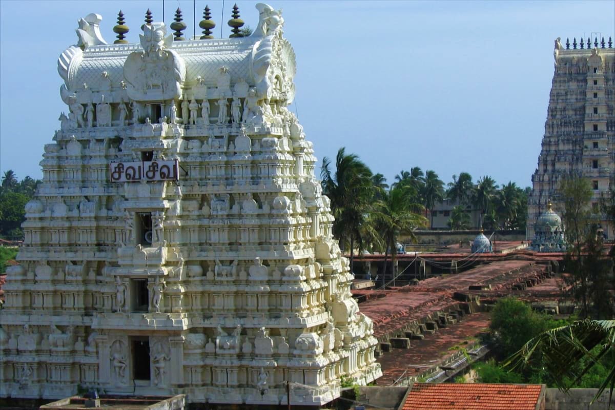 White ornate Hindu temple tower with intricate carved sculptures and palm trees in background at Indian religious site