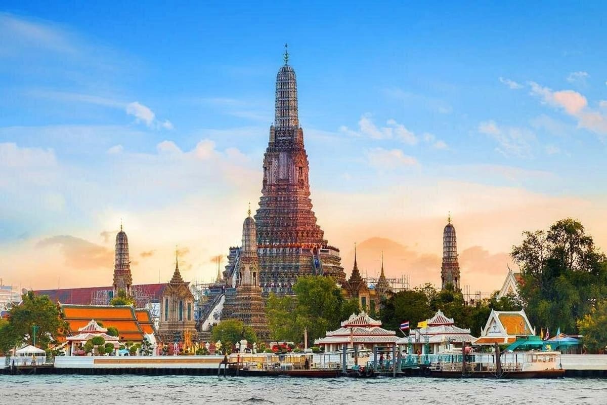 Best of Bangkok and Pattaya Wat Arun temple with ornate spires along the Chao Phraya River in Bangkok, Thailand at sunset with traditional boats