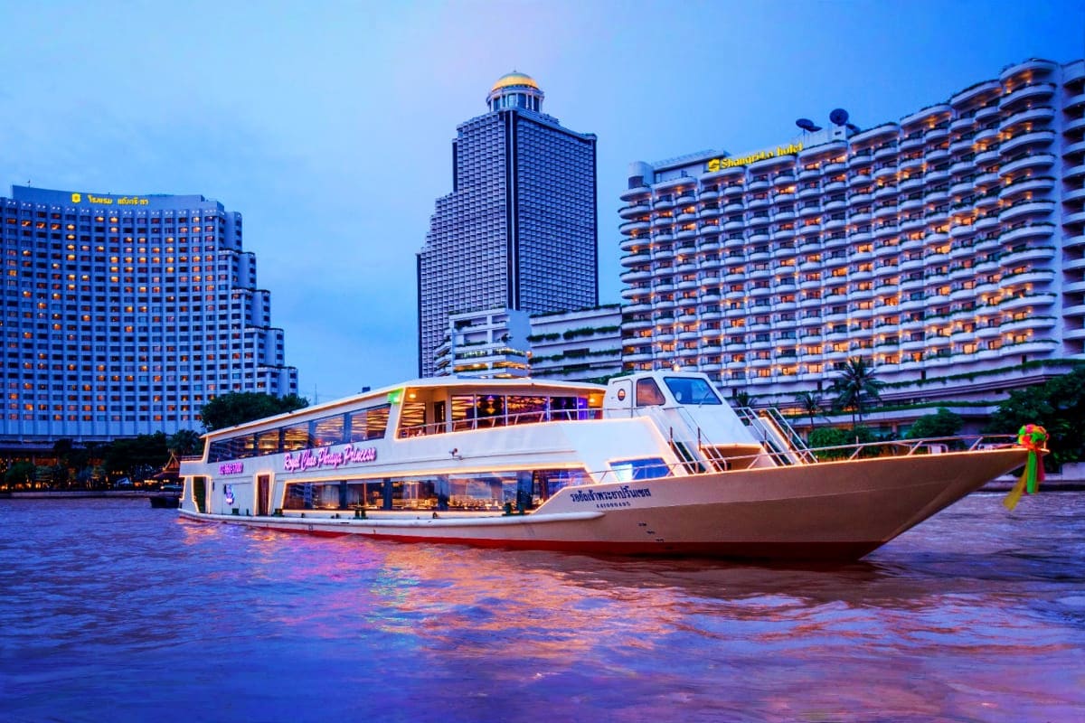 White passenger ferry boat on the Chao Phraya River at dusk with illuminated high-rise hotels and office buildings in Bangkok
