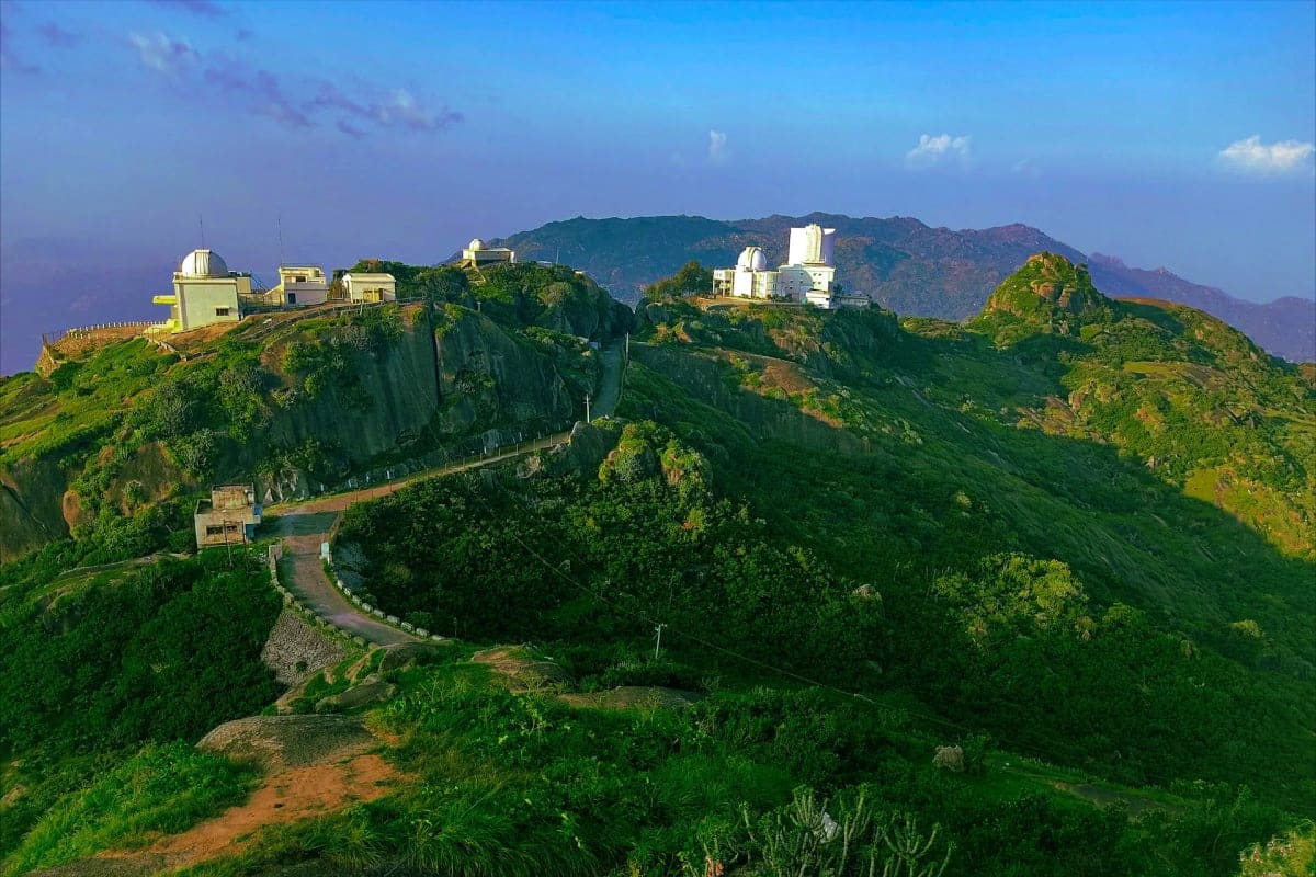 Observatory buildings and white structures perched on rocky hilltops surrounded by lush green vegetation and mountains in the
