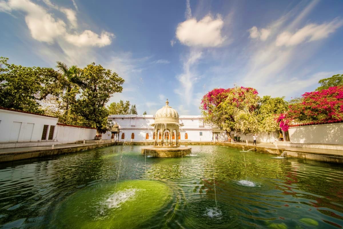 Historic white palace with golden domed structure reflected in serene green water, surrounded by vibrant pink flowering vines