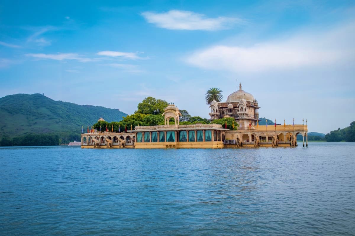 Jag Mandir Palace floating on Lake Pichola in Udaipur with yellow sandstone architecture and palm trees against blue sky and 