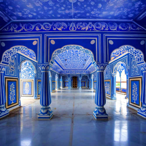 Ornate blue and white corridor with decorated arches, pillars, and intricate floral patterns in traditional Indian palace arc