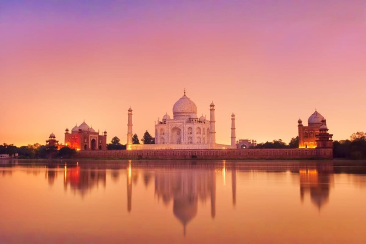 Taj Mahal illuminated at sunset reflected in the Yamuna River with pink and golden sky, Agra India