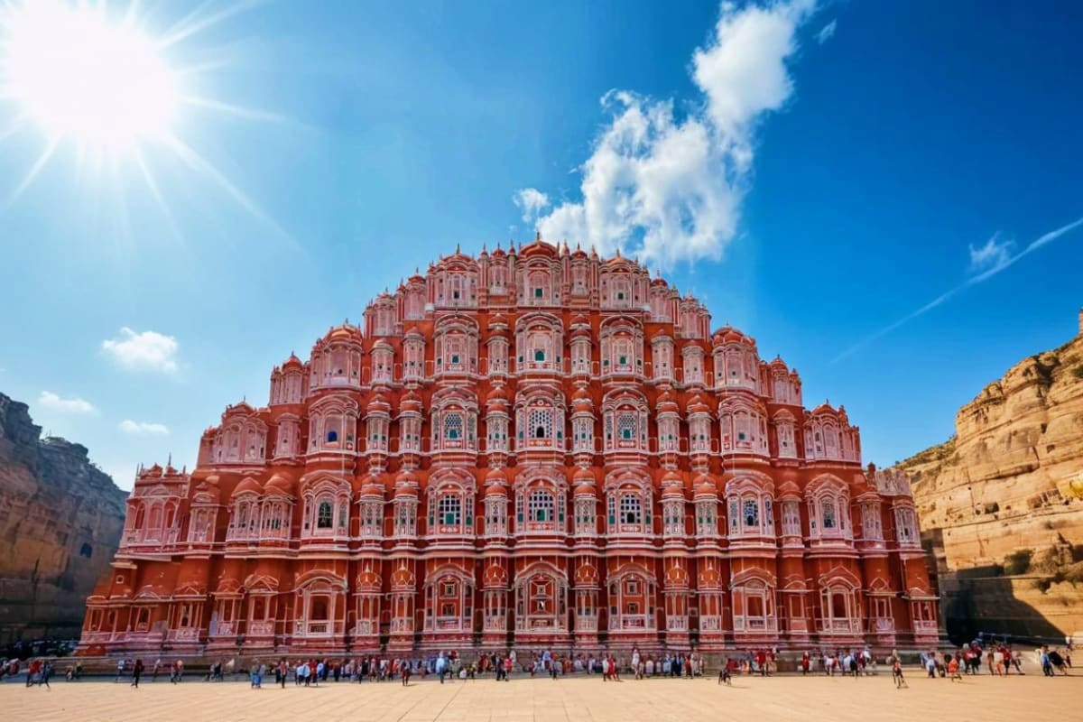 Hawa Mahal pink palace in Jaipur with tourists gathered in courtyard under clear blue sky and bright sun