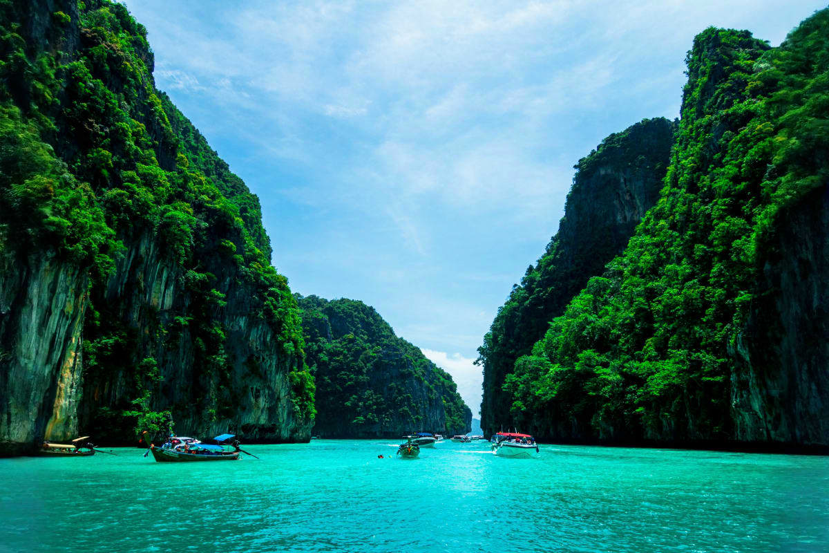 Turquoise lagoon surrounded by tall limestone cliffs with traditional longtail boats, Phi Phi Islands Thailand