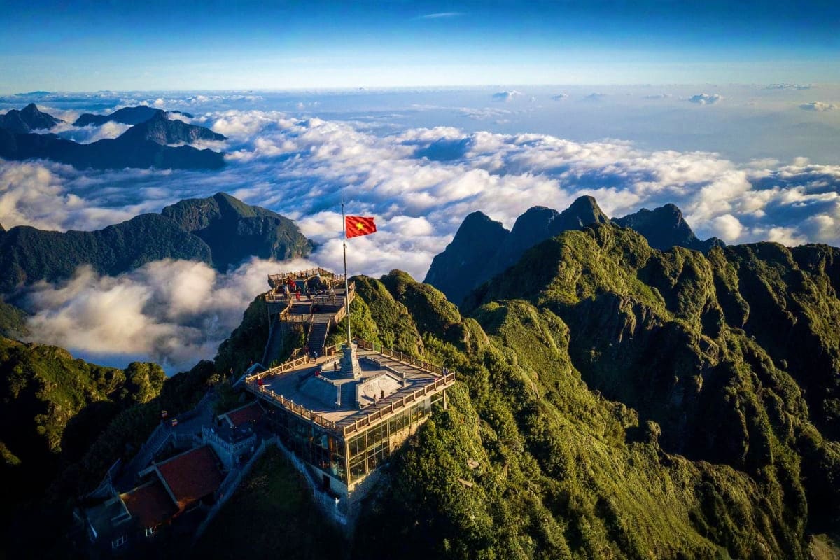 Mountain temple with Vietnamese flag overlooking sea of clouds and forested peaks in Sapa, Vietnam