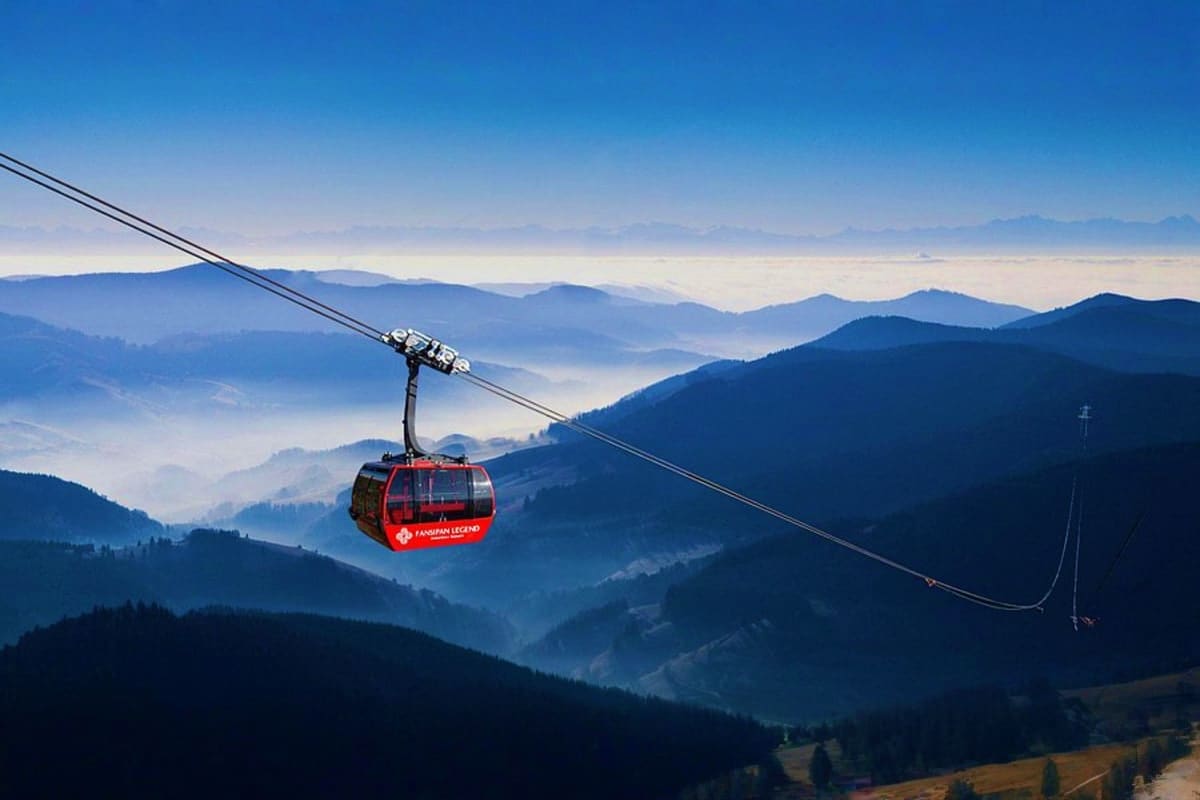 Red cable car suspended over misty mountain valley with forested peaks and morning fog in Sapa, Vietnam