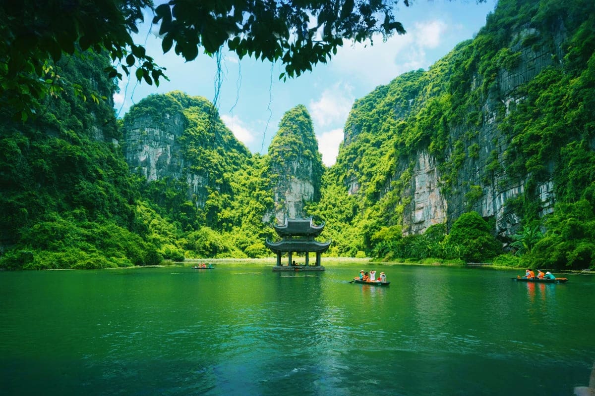 Traditional pagoda temple on emerald river surrounded by dramatic limestone cliffs and lush green vegetation in Vietnam karst