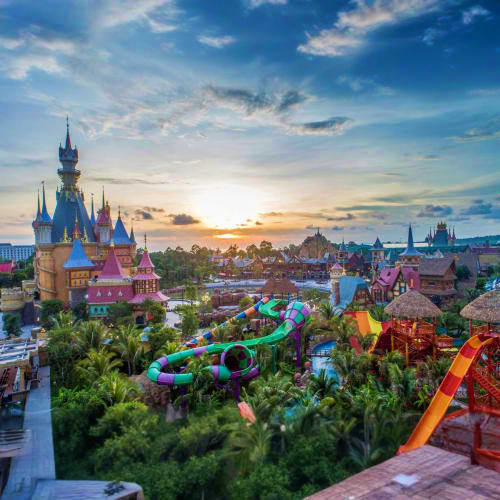 Fairy tale castle with colorful water slides and tropical gardens at sunset in theme park