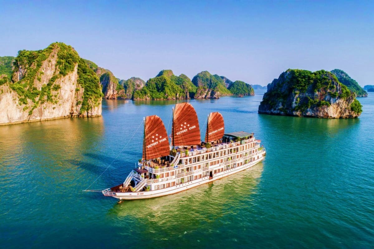 Traditional junk boat with red sails sailing through limestone karst islands in Halong Bay, Vietnam