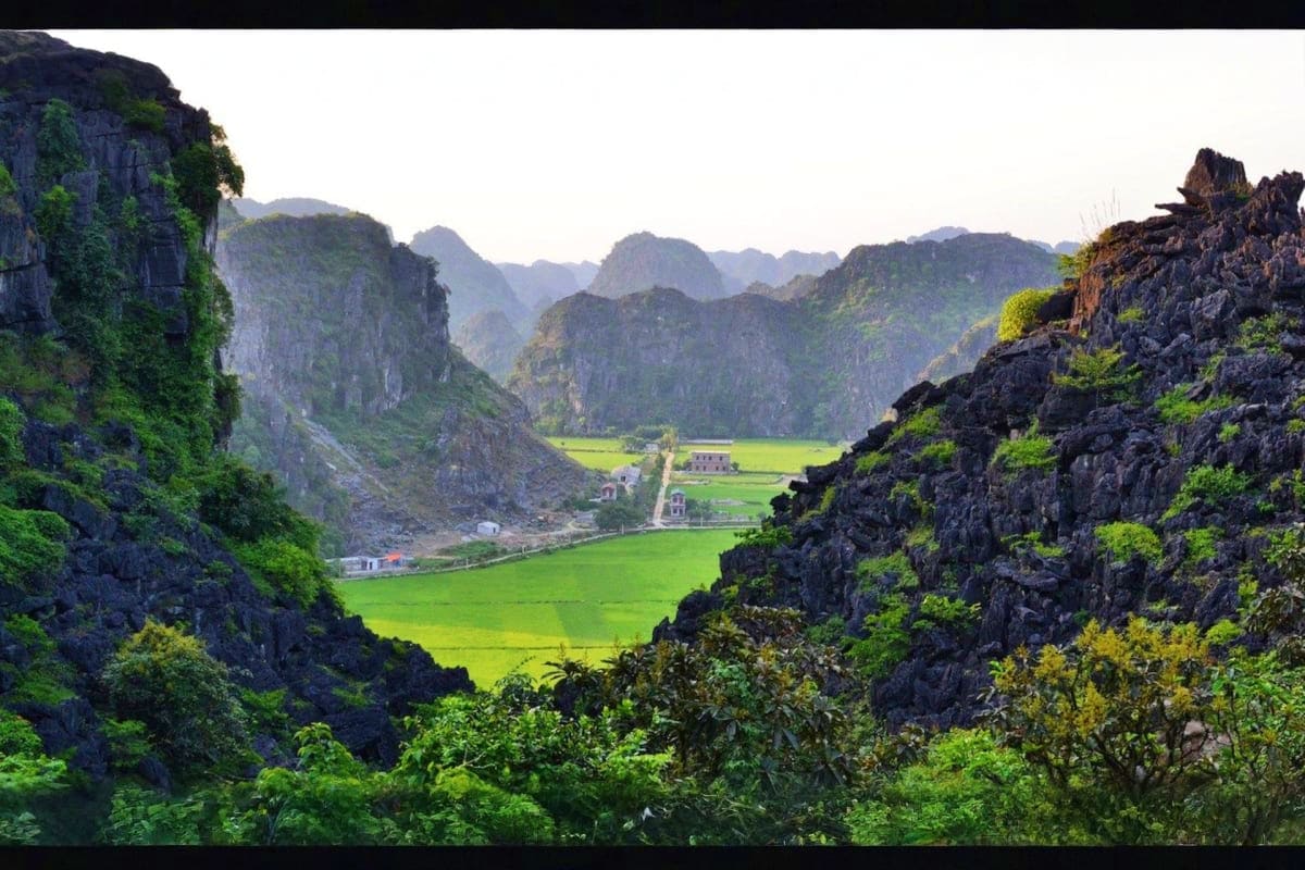 Limestone karst mountains surrounding lush green valley with rice fields and traditional buildings in Ninh Binh, Vietnam