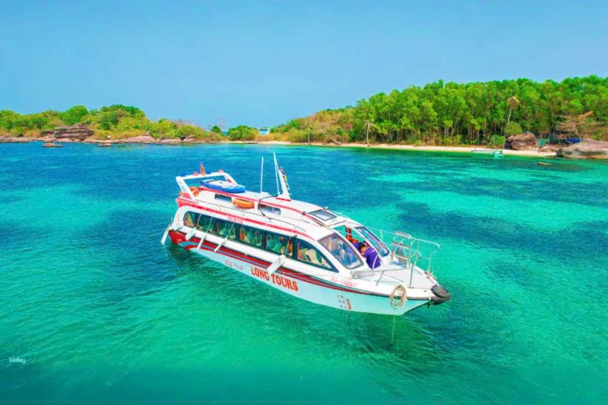 Tour boat anchored in turquoise waters with forested coastline and beach in background, Vietnam